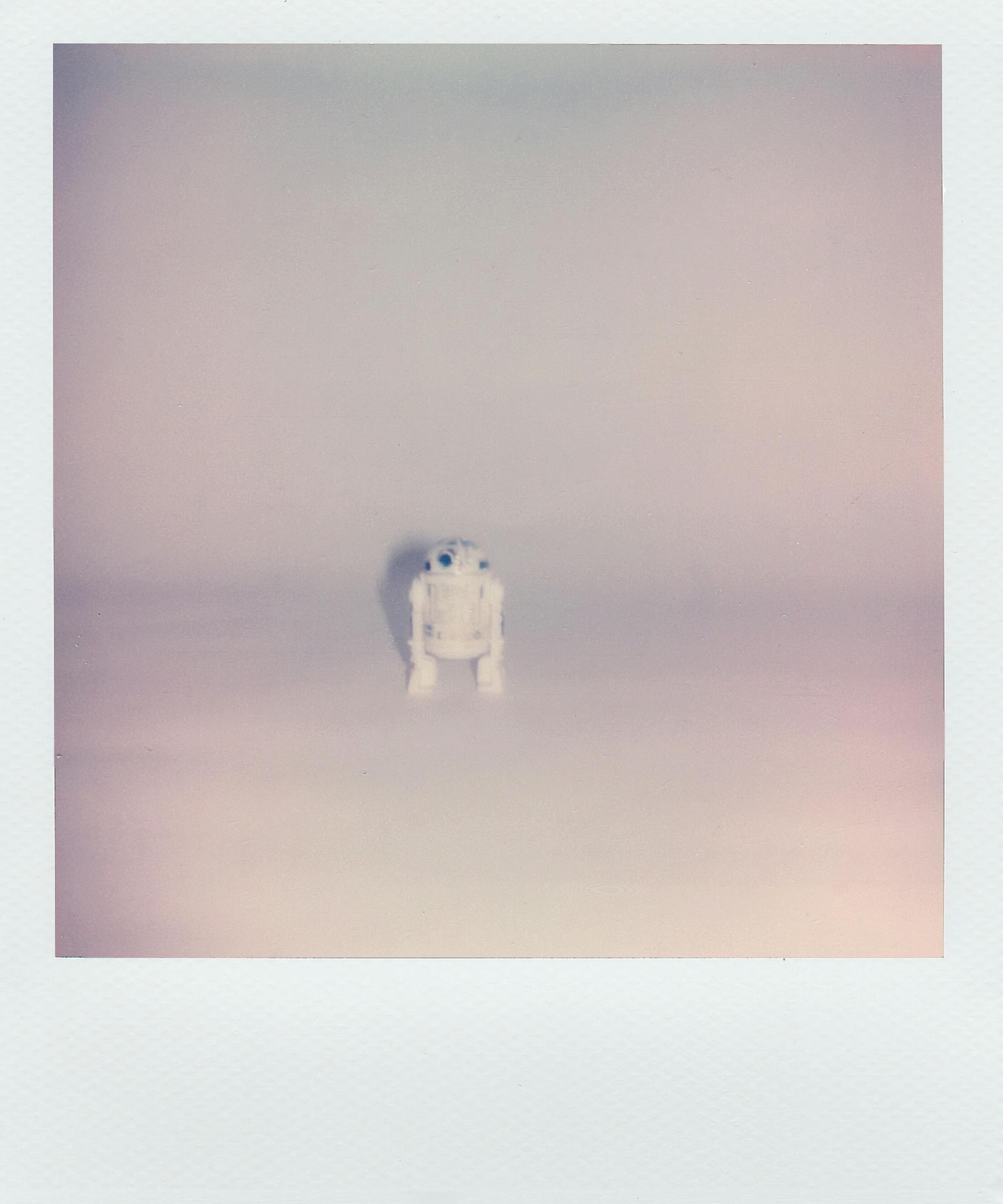 A lone toy robot stands against a soft, minimalist white backdrop.